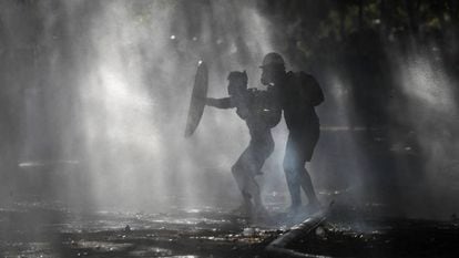 Manifestantes se defendem dos jatos d’água com os quais a polícia tenta dispersá-los, durante um protesto em Santiago.