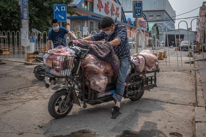 Homens com máscaras protetoras carregam uma moto com carne do lado de fora do mercado Xinfadi, em Pequim.