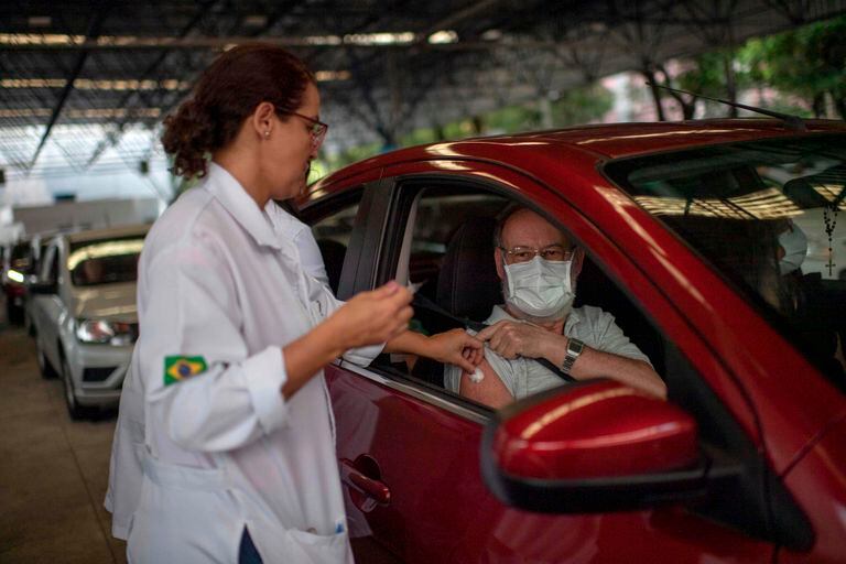 A Public Health worker gives a flu vaccine to a man at a drive-through model in Tijuca neighbourhood in Rio de Janeiro, Brazil, on March 24, 2020. - The Rio de Janeiro state government is requesting people not to go to the beach or any other public areas as a measure to contain the coronavirus pandemic. (Photo by Mauro PIMENTEL / AFP)