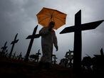 Un trabajador con traje de protección y paraguas pasa por delante de las tumbas de las víctimas por el COVID-19 en el cementerio de Nossa Senhora Aparecida, en Manaos, Brasil, el 25 de febrero de 2021. - Brasil superó las 250.000 muertes por efectos del coronavirus.