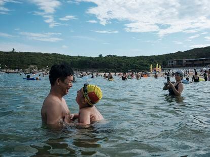 Uma criança com uma touca de natação com a bandeira da China é vista com o pai, na praia de Dongchong.