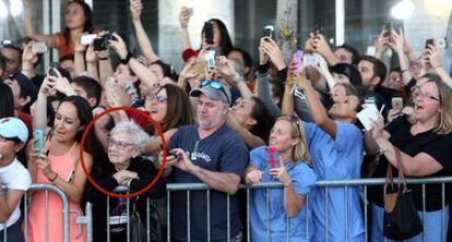 Idosa observa atores enquanto público tenta fotografá-los.