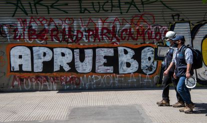 Homens passam diante de um grafite em Santiago do Chile que convoca a população a votar em favor da reforma constitucional no próximo domingo.