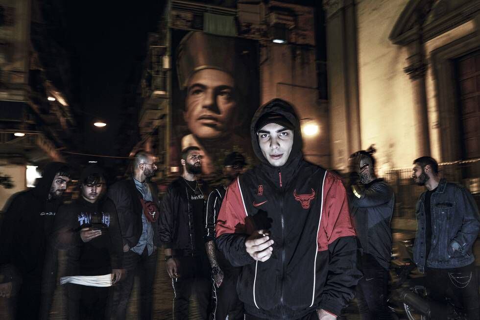 Um grupo de jovens do bairro de Forcella reunido na noite napolitana sob o mural com a imagem de San Gennaro, obra do artista Jorit.