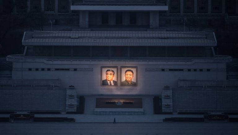 Homem passeia sob os dois grandes retratos de Kim Il-sung (esq.) e Kim Jong-il (dir.) em Pyongyang.