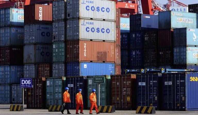 Três trabalhadores diante de vários contêineres no porto de Qingdao, leste da China.
