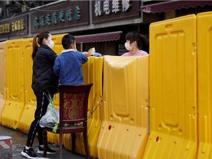 Uma mulher paga a compra de um mercado delimitado por uma barreira levantada durante a quarentena, em Wuhan.
