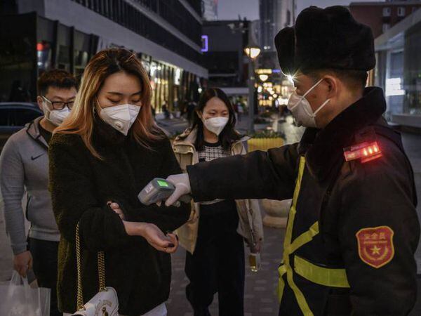 Clientes de un centro comercial en Beijing, China, sometiéndose a un control antes de acceder.