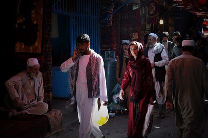 Uma mulher caminha entre homens pelas ruas do bazar Mandawi, em Cabul.