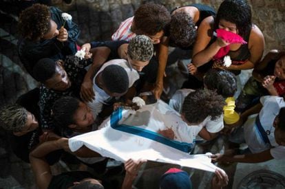 Amigos e familiares de Marcos Vinícios choram sobre sua camiseta da escola manchada de sangue, durante o seu velório.