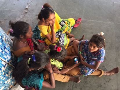 Um grupo de garotas se reúne ao redor de um telefone em uma estação de trens de Bombaim.