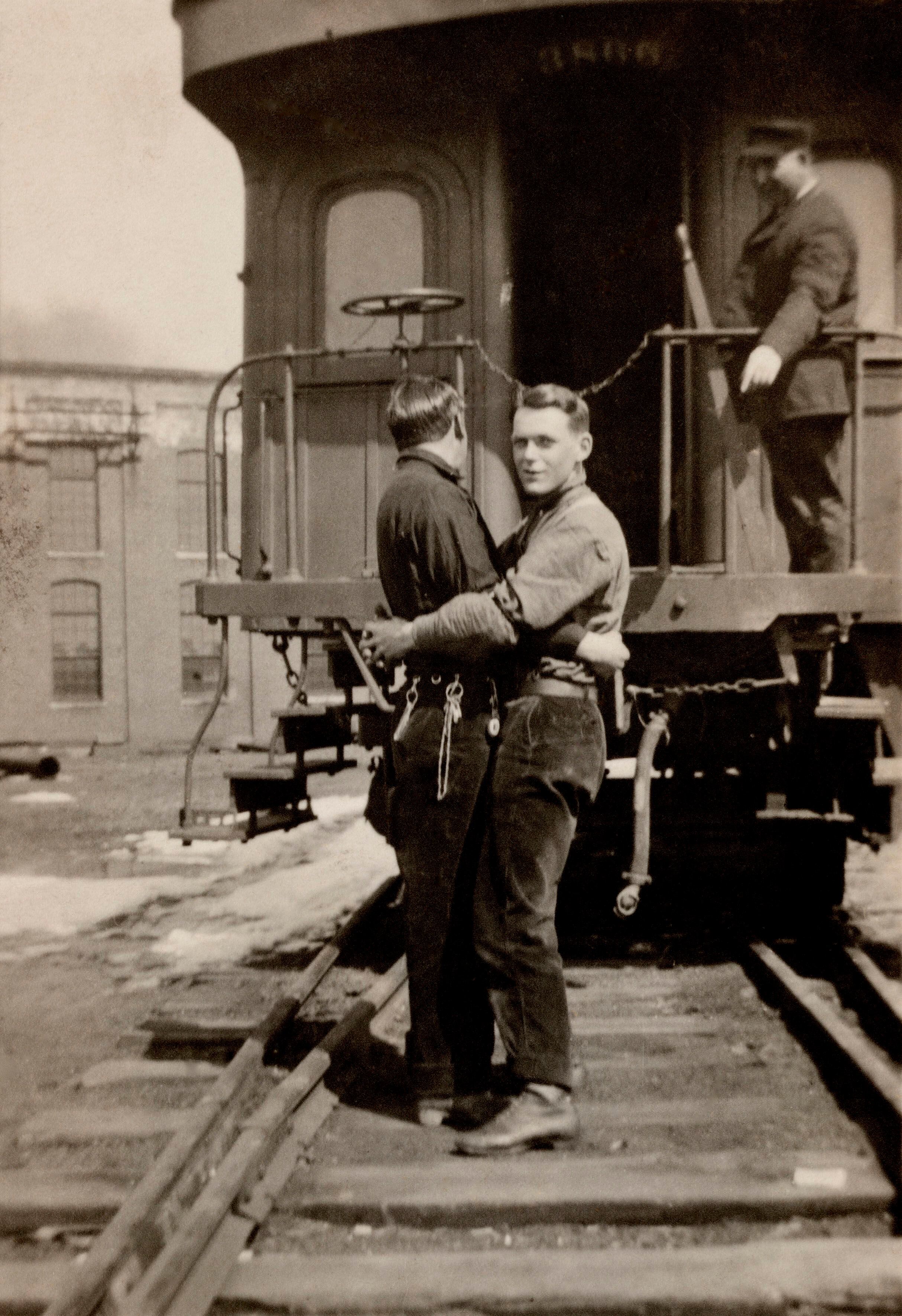 Um casal se abraça, ao fundo há um trem com um maquinista que os observa. A data da foto é desconhecida, mas se sabe que é uma imagem estadounidense. 
