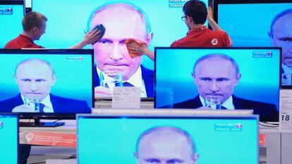 Funcionários de uma loja limpam uma tela de televisão durante pronunciamento do presidente Vladimir Putin, na quinta-feira, em Moscou.