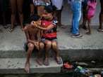 Uma menina ajuda um menino a colocar uma máscara doada enquanto os moradores fazem fila para receber sacolas de comida grátis, no Rio de Janeiro.