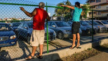 Cubanos observam um pátio com carros usados à venda.
