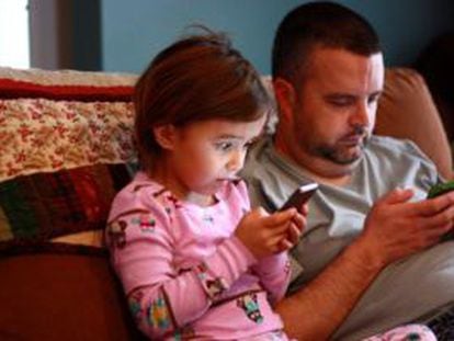 Uma menina e seu pai concentrados nos celulares.