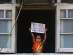 A girl dressed in traditional attire to celebrate "Gudi Padwa", or the Marathi New Year, stands by a window and holds a placard with an acronym for the Coronavirus that reads in hindi "Nobody should come out on the roads," in Mumbai, India, Wednesday, March 25, 2020. The world's largest democracy went under the world's biggest lockdown Wednesday, with India's 1.3 billion people ordered to stay home in a bid to stop the coronavirus pandemic from spreading and overwhelming its fragile health care system as it has done elsewhere. For most people, the new coronavirus causes mild or moderate symptoms, such as fever and cough that clear up in two to three weeks. For some, especially older adults and people with existing health problems, it can cause more severe illness, including pneumonia and death. (AP Photo/Rafiq Maqbool)