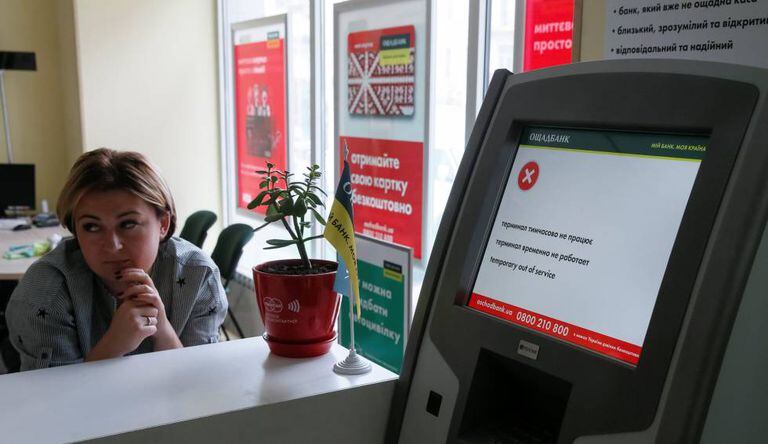 Uma funcionária do banco Oschadbank junto a um caixa afetado pelo vírus em Kiev.