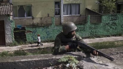 Uma menina passa por um soldado armado, durante uma operação surpresa na Cidade de Deus, no Rio de Janeiro.