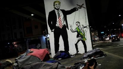 Sem-teto diante de grafite que ironiza a relação de Trump e Bolsonaro.