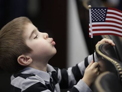 Menino brinca com bandeira dos EUA durante cerimônia de naturalização da mãe.