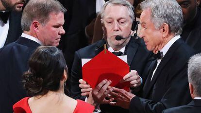Brian Cullinan (à esquerda e com expressão séria), da PriceWaterHouseCoopers, fala com Warren Beatty no palco. De costas, de vestido vermelho, a outra auditora da PWC, Martha Ruiz.