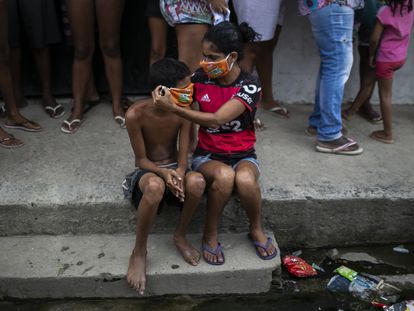 Uma menina ajuda um menino a colocar uma máscara doada enquanto os moradores fazem fila para receber sacolas de comida grátis, no Rio de Janeiro.