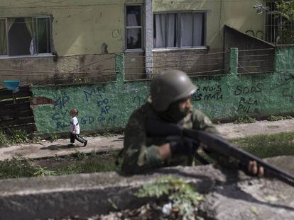 Uma menina passa por um soldado armado, durante uma operação surpresa na Cidade de Deus, no Rio de Janeiro.