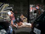 A homeless man sleeps in the street as passers-by walk wearing face masks during the first day of lockdown due to the COVID-19 coronavirus, in Niteroi, Rio de Janeiro state, Brazil, on May 11, 2020. - Brazil, the hardest-hit Latin American country in the coronavirus pandemic, has surpassed 10,000 deaths, according to figures released last weekend by the Ministry of Health. (Photo by Mauro Pimentel / AFP)