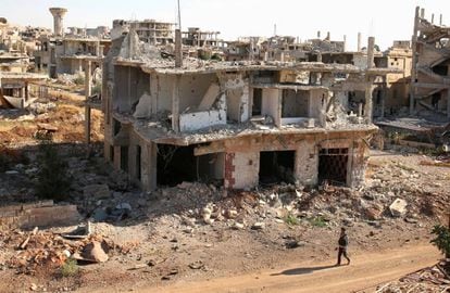 Um rebelde caminha em frente a construções destruídas na parte rebelde de Deraa.