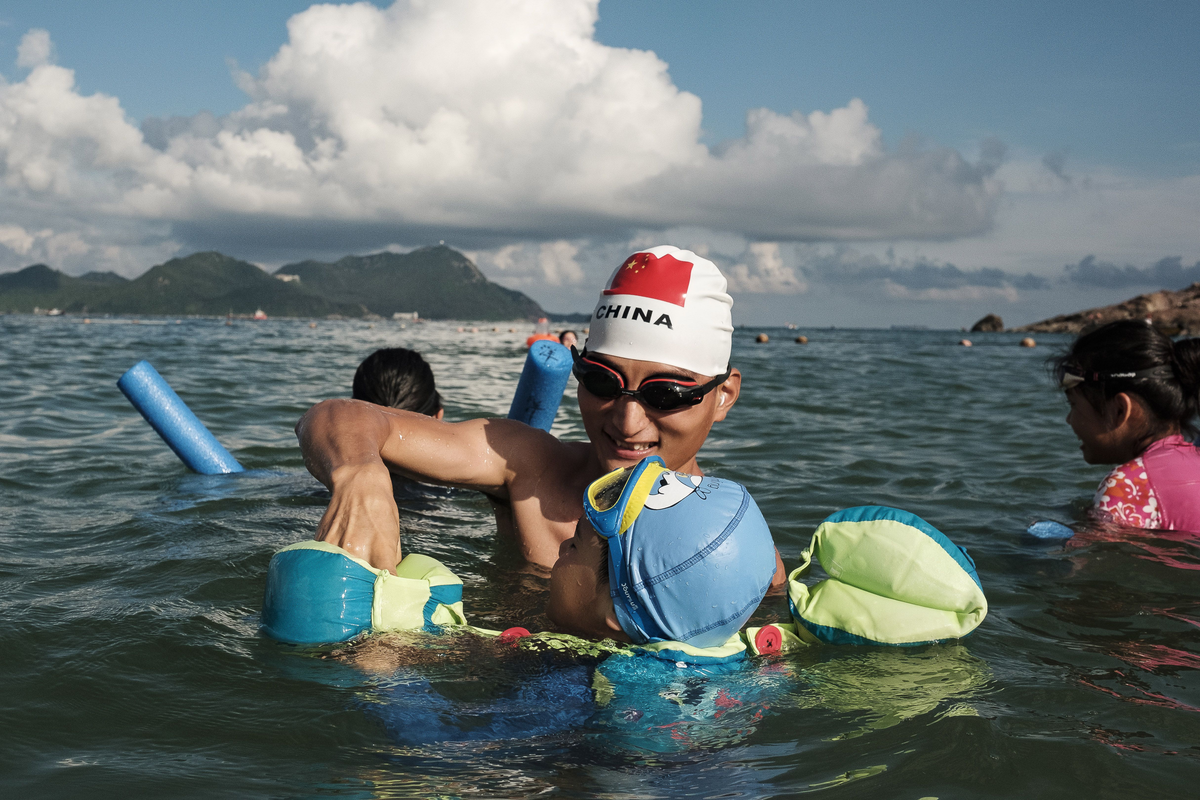 Uma banhista, com uma touca de natação com a bandeira da China, ajuda uma criança a usar uma boia na praia de Dongchong. 