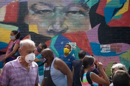 Pedestres caminham diante de mural que retrata o ex-presidente Hugo Chávez em Caracas, em 2 de julho.