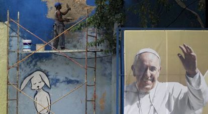 Um operário conserta um muro junto a um cartaz do Papa.