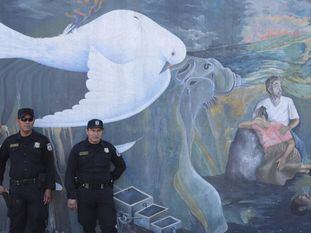 Policiais salvadorenhos diante de um mural que faz alusão à guerra civil de El Salvador (1980-92).