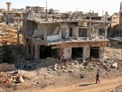 Um rebelde caminha em frente a construções destruídas na parte rebelde de Deraa.