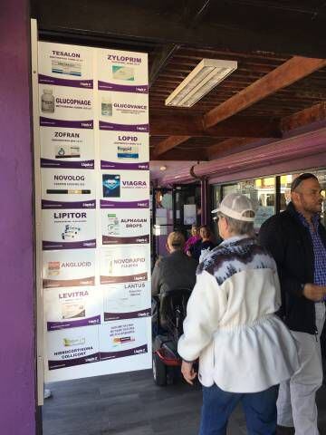Turistas ao lado de anúncios de medicamentos em uma farmácia em Los Algodones, Baixa Califórnia