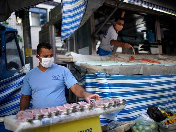 Men wearing face masks arrange fish for sale after street markets were reopened in Rio de Janeiro, Brazil on April 29, 2020, amid the new coronavirus pandemic. - Rio de Janeiro's municipality authorized the reopening of street markets but under safety measures as the use of alcohol gel, face masks and keeping a distance of two meters between each stand. (Photo by Mauro Pimentel / AFP)