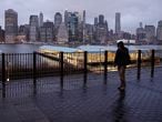 A person walks on an empty sidewalk as rain clouds hang over the downtown Manhattan skyline, Tuesday, March 17, 2020, in New York.  (AP Photo/John Minchillo)
