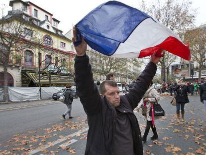 Um homem ergue a bandeira da França em frente ao Bataclan.