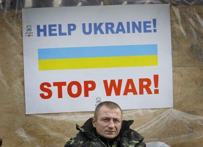 Um veterano do Maidan ante um cartaz que diz: "Ajudem a Ucrania, parem a guerra".