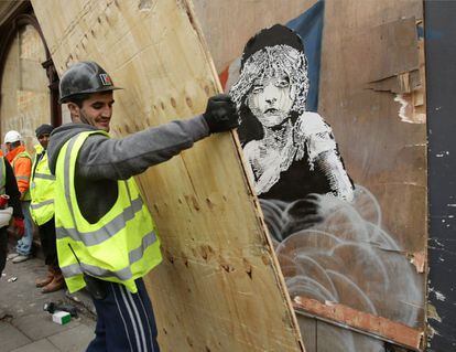 Um homem cobre hoje com uma tábua de madeira o grafiti de Banksy ante a Embaixada da França em Londres.