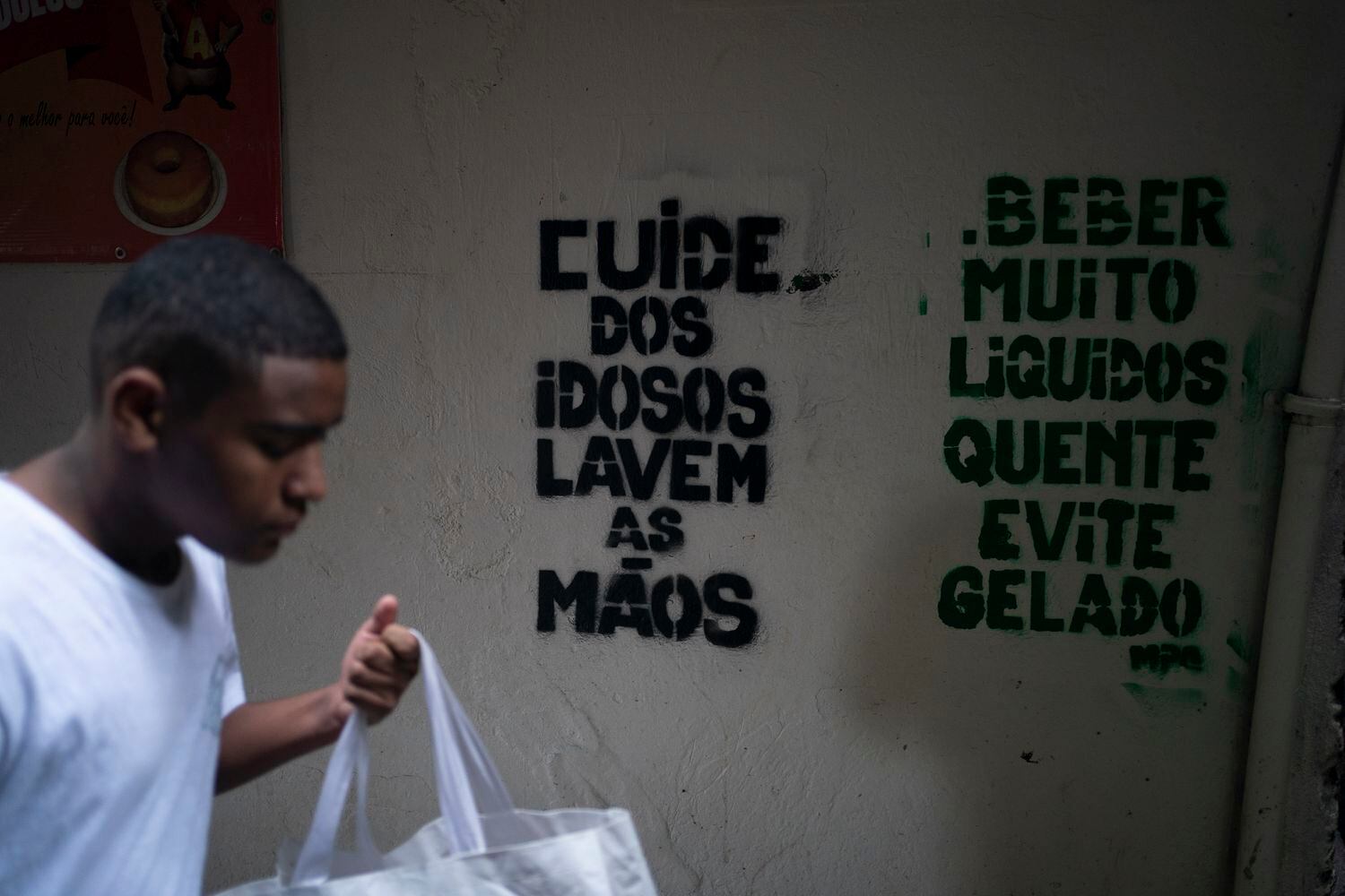 Um homem passa em frente a recados de conscientização sobre o coronavírus na Rocinha, Rio de Janeiro.