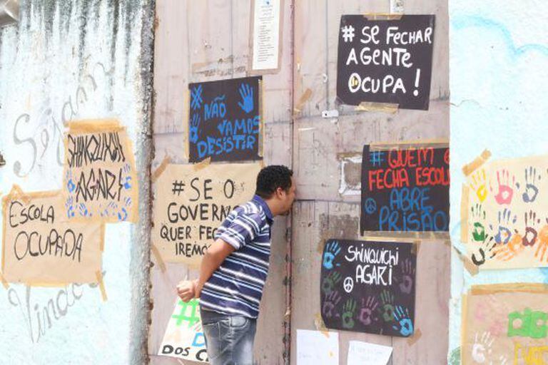 Homem olha pelo portão de uma escola ocupada.