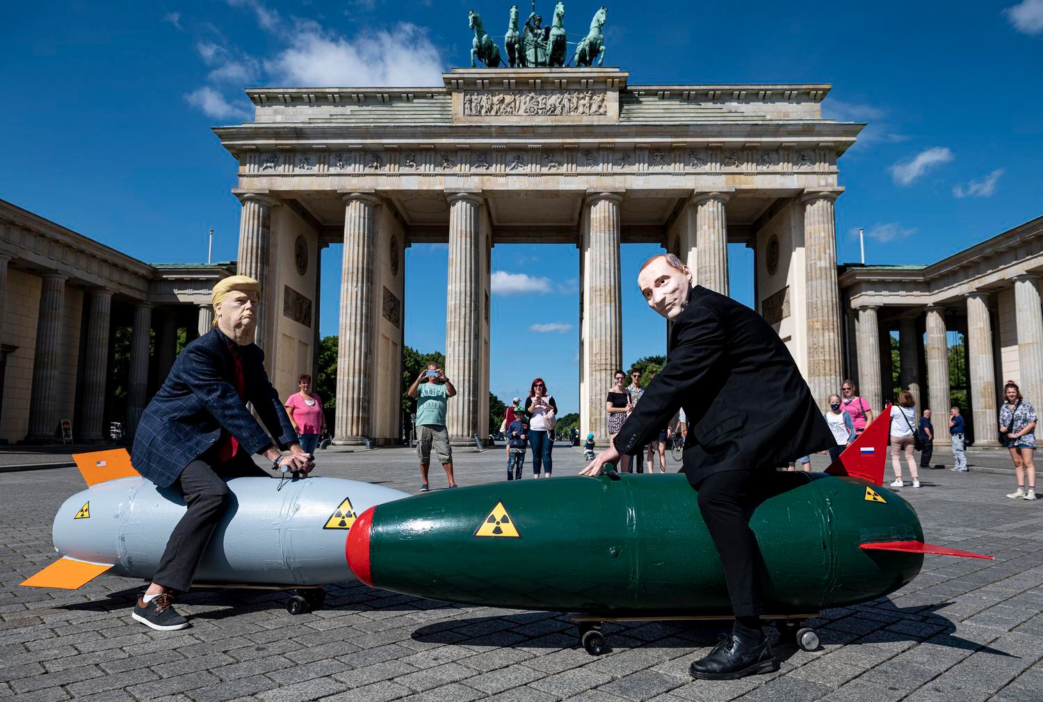Manifestantes com máscaras de Trump e Putin posam sobre duas bombas falsas durante protesto contra armas atômicas em Berlim, na Alemanha.