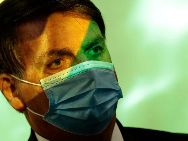 Brazil's President Jair Bolsonaro wears a mask amid the COVID-19 pandemic at the start of a ceremony where his nation's flag is projected over him in Brasilia, Brazil, Wednesday, Aug. 5, 2020. In May, facing urgent international demands for action after a string of massive wildfires in the Amazon, Brazilian President Jair Bolsonaro put the army in charge of protecting the rainforest. (AP Photo/Eraldo Peres)