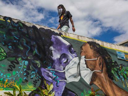 Homem com máscara passa por graffiti de Marcos Costa, o Spray Cabuloso, na entrada da favela Solar de Unhão em Salvador, Bahia, em 15 de abril.