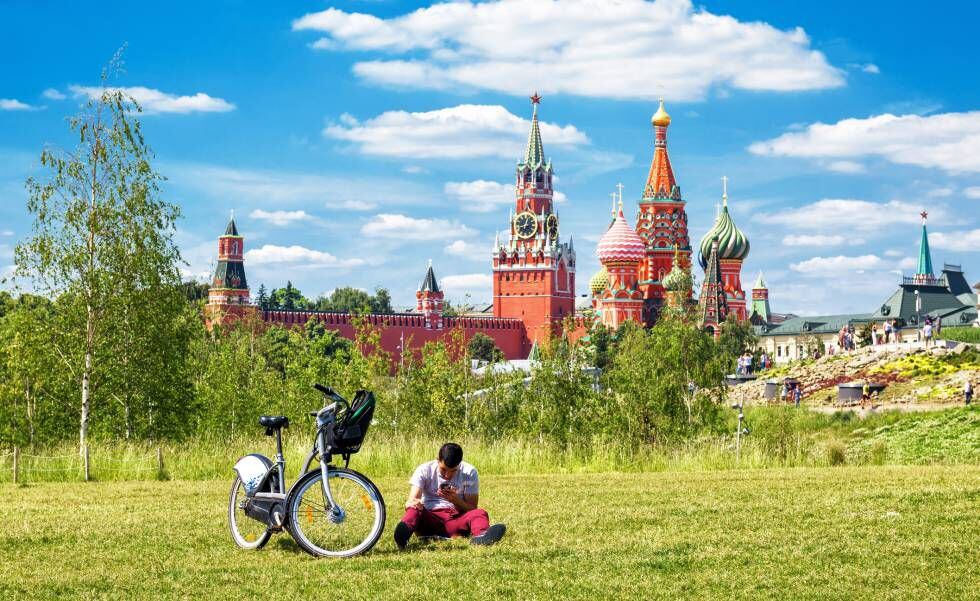 Ciclista urbano descansa no parque Zaryadye, em Moscou, com o Kremlin e a catedral de São Basílio ao fundo.