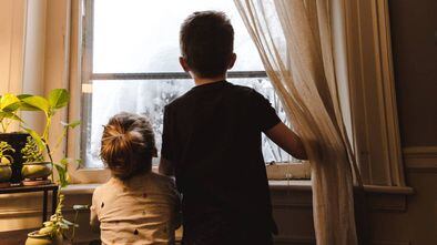 Duas crianças olham por uma janela. Quarentena impõe desafio para pais e filhos.