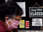 (FILES) In this file photo taken on May 4, 2020, a woman wearing a face mask walks past a sign in the window of a food store announcing that the business is closed during a shelter in place lockdown order during an outbreak of COVID-1 in Arlington, Virginia. - The global coronavirus pandemic has sparked an economic "crisis like no other," sending world GDP plunging 4.9 percent this year and wiping out $12 trillion over two years, the IMF said June 24, 2020. Worldwide business shutdowns destroyed hundreds of millions of jobs, and major economies in Europe face double-digit collapses.The prospects for recovery post-pandemic -- like the forecasts themselves -- are steeped in "pervasive uncertainty" given the unpredictable path of the virus, the IMF said in its updated World Economic Outlook. (Photo by Olivier DOULIERY / AFP)