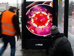 Two man wait at a bus stop with a screen displaying a symbol photo of the novel coronavirus in Berlin, Germany, Thursday, March 12, 2020. The display is an advertisement for a free health magazine provide by German pharmacies. For most people, the new coronavirus causes only mild or moderate symptoms, such as fever and cough. For some, especially older adults and people with existing health problems, it can cause more severe illness, including pneumonia.(AP Photo/Markus Schreiber)